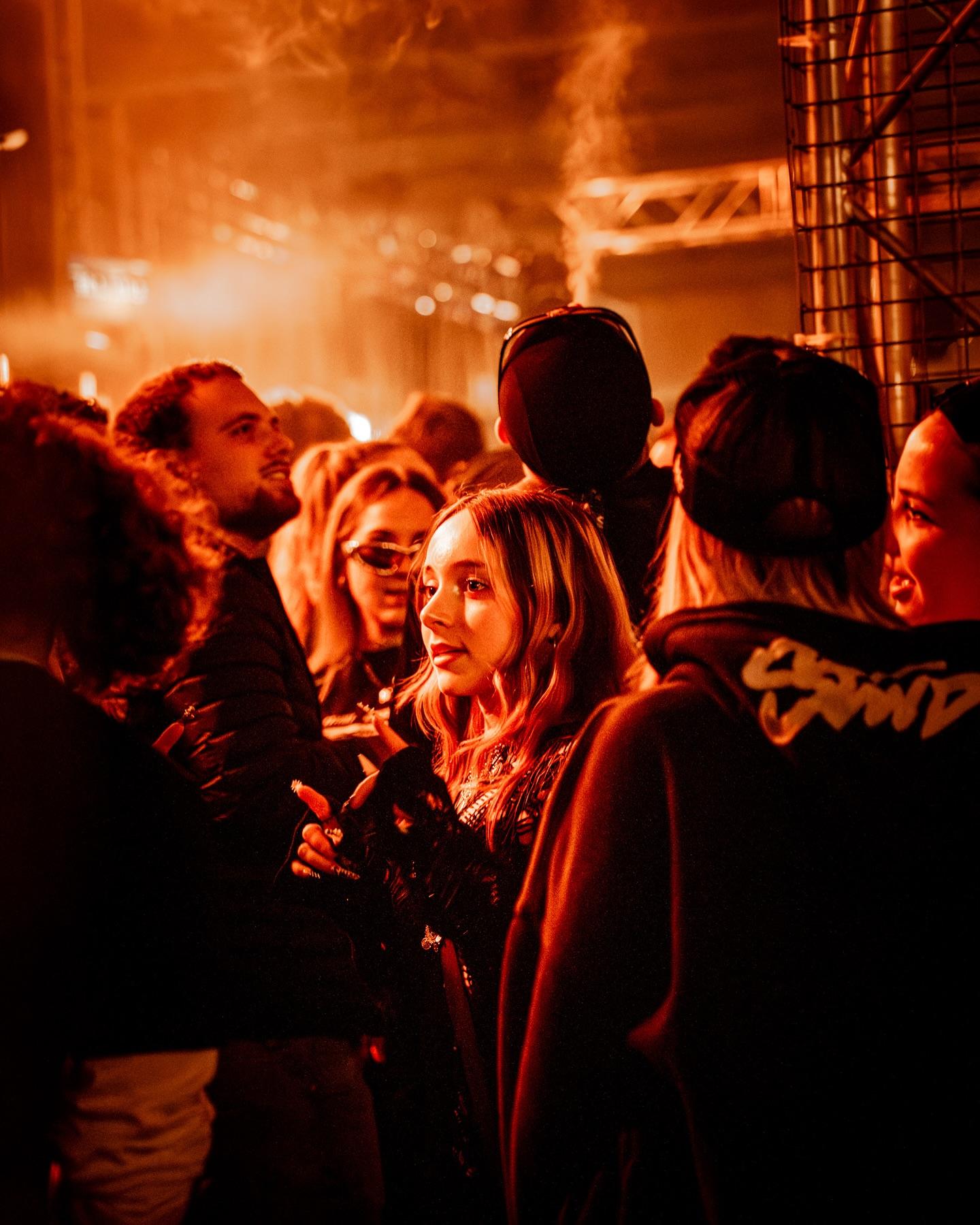 A warm orange crowd gathered beneath stage truss and smoke
